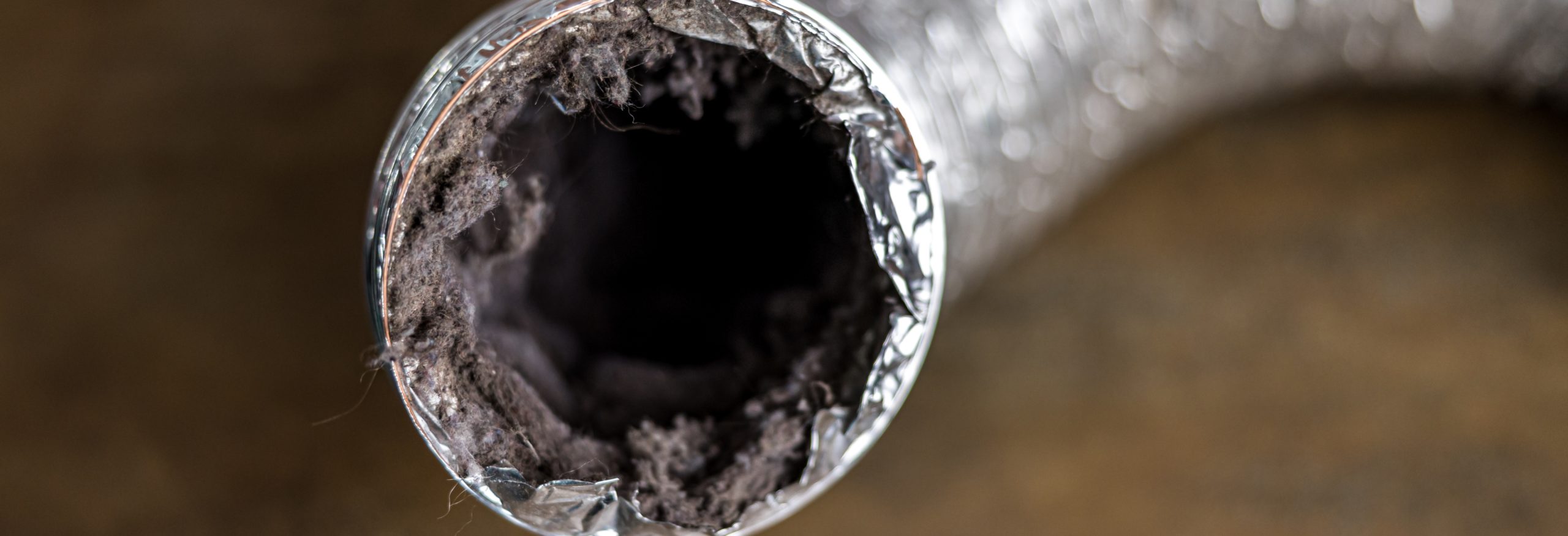 Close-up photo of a silver dryer vent tube with lint stuck inside.