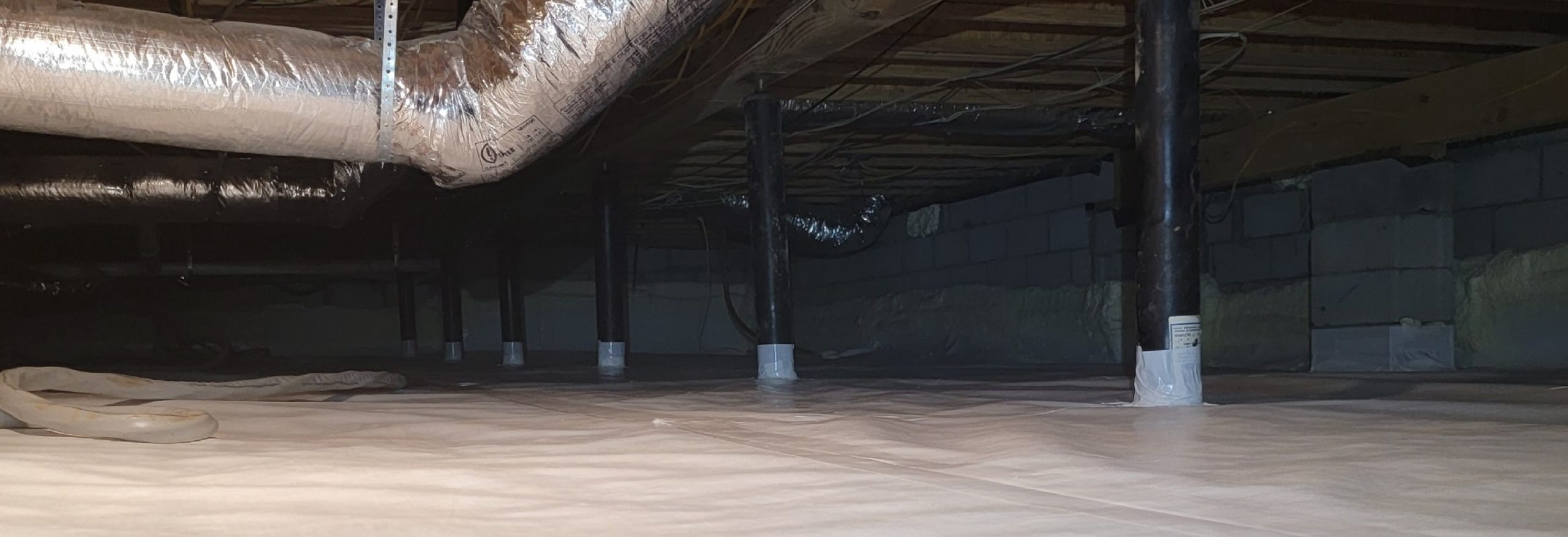 Panoramic photo of a crawl space with vapor barrier being installed.