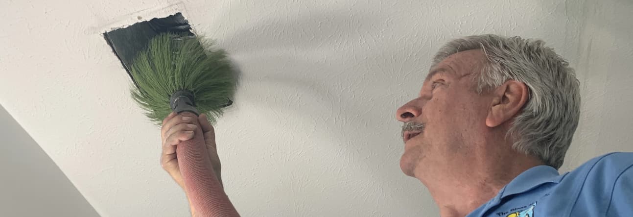 Photo of a man cleaning an air vent with a duster with green bristles.